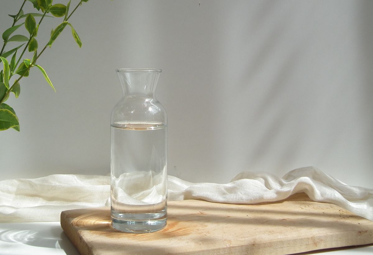 Carafe en verre remplie d'eau claire sur une planche en bois, lumière naturelle