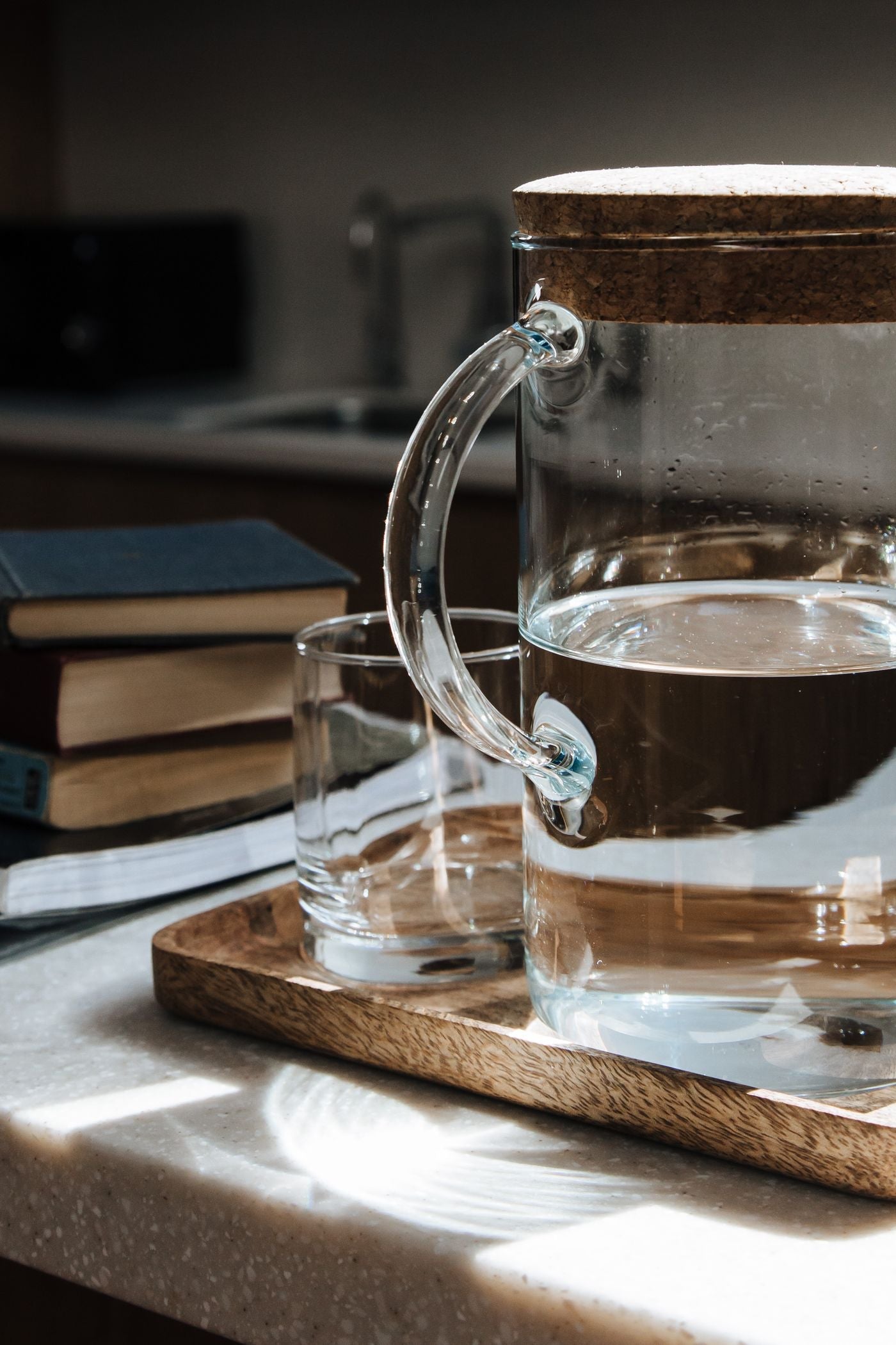 Carafe en verre remplie d'eau claire et son verre, posés sur un plateau en bois, lumière douce