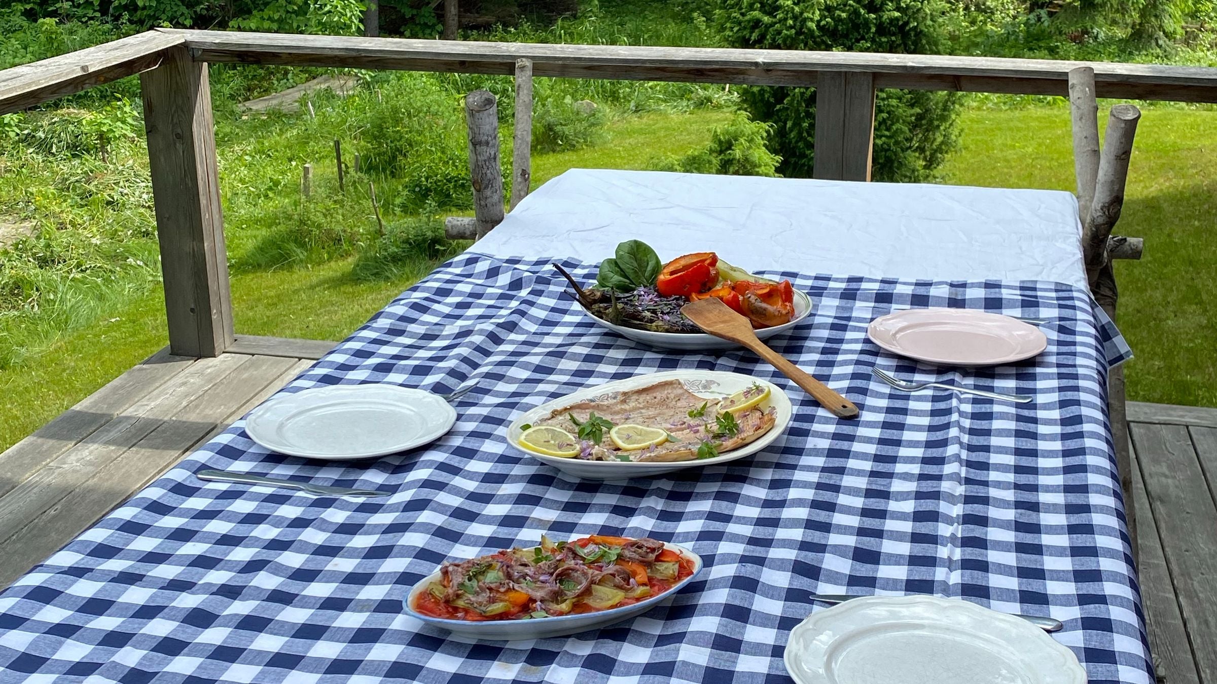 Table de terrasse dressée avec une nappe vichy bleu et blanc, plats d'été et vaisselle claire