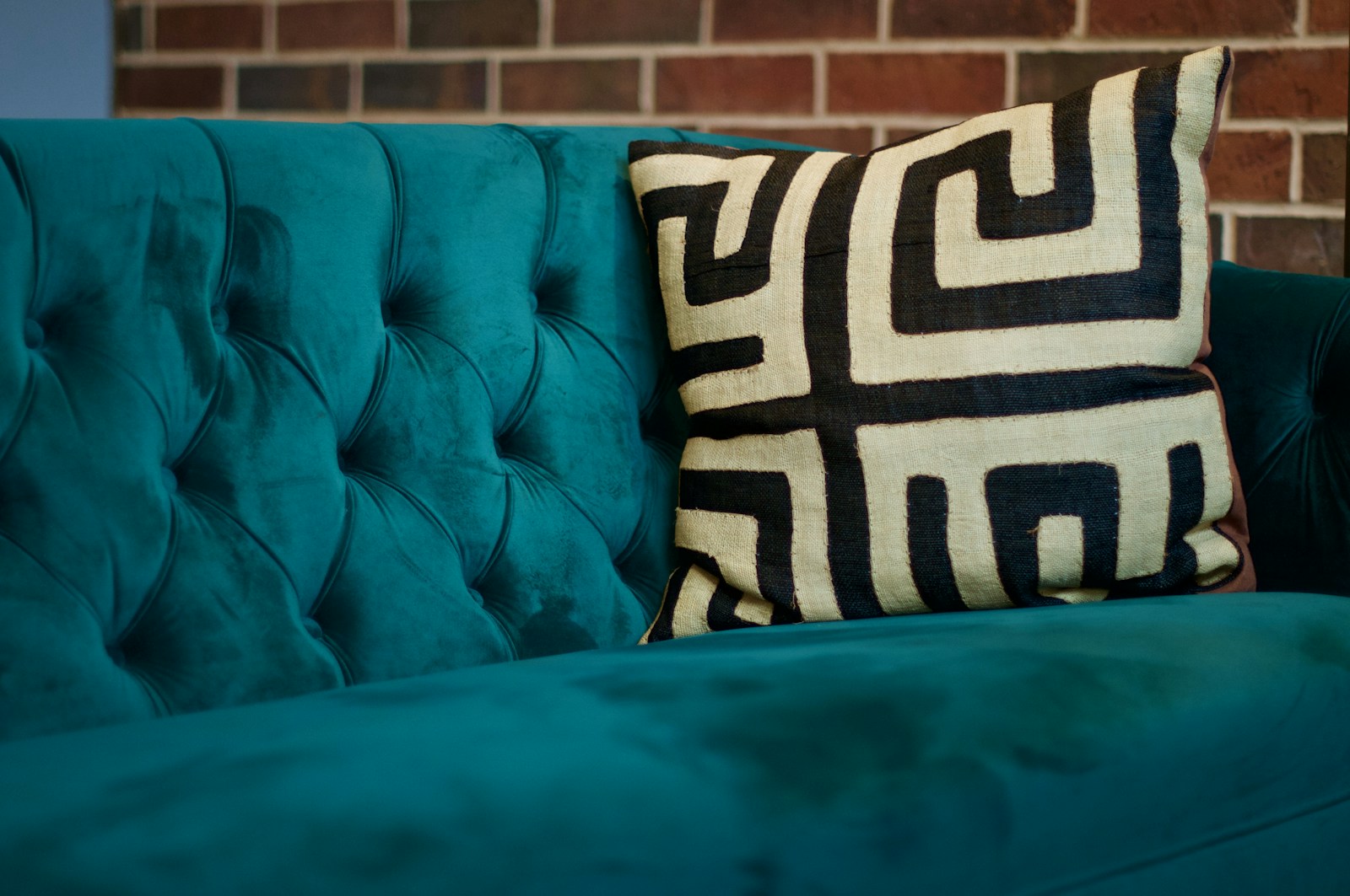 Canapé en velours teal avec coussin graphique dans un salon chaleureux