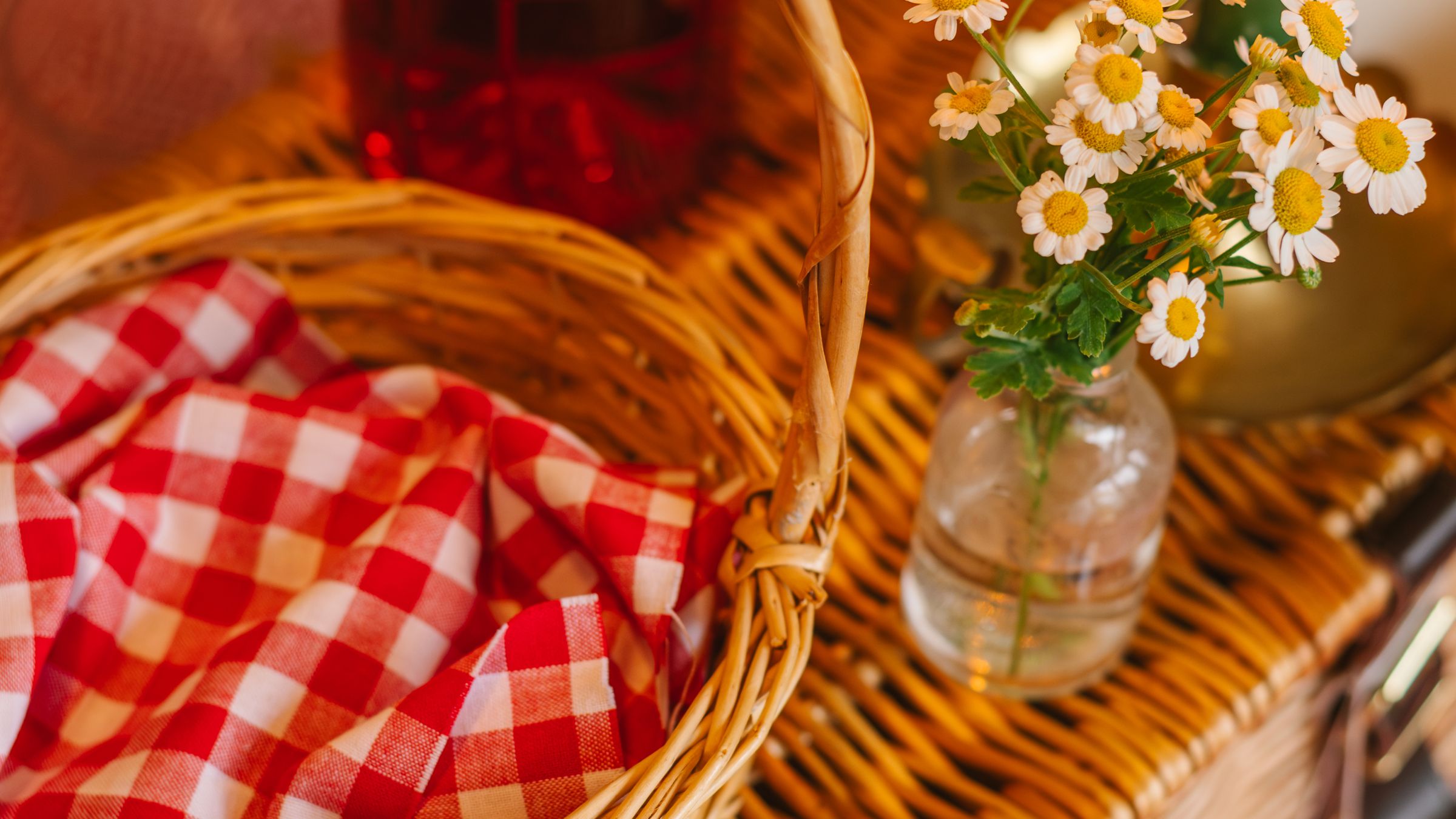 Panier de pique-nique en osier avec nappe vichy rouge et blanche et bouquet de marguerites