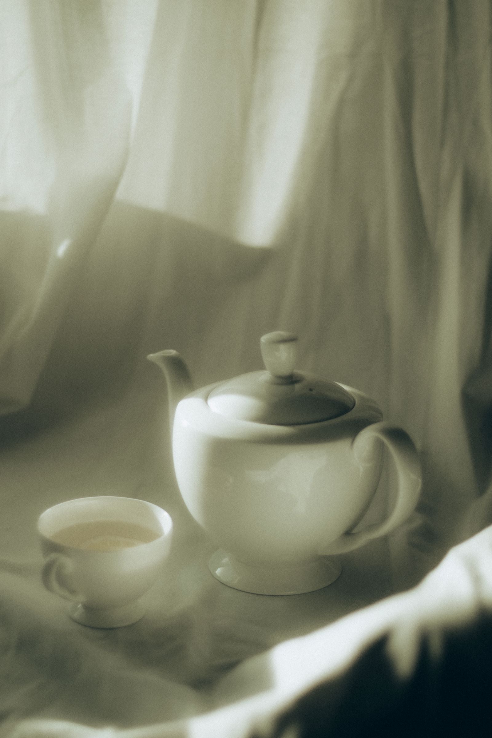 Théière céramique blanche et tasse de thé fumant sur nappe en lin, lumière naturelle, art de la table