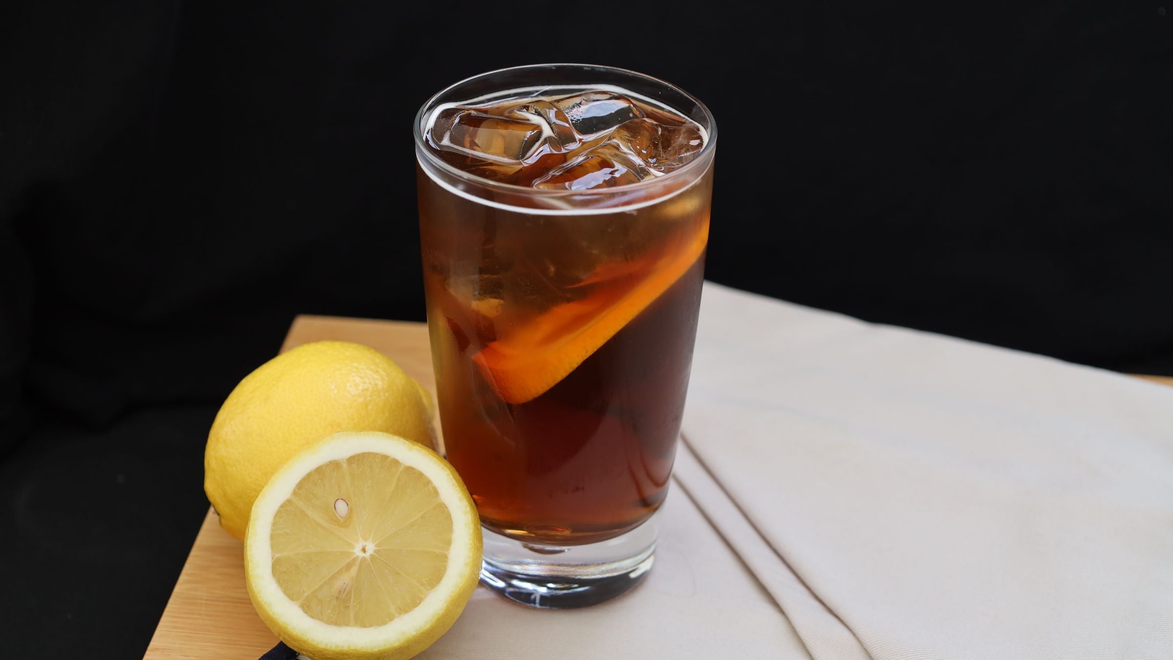 Verre de thé glacé maison avec glaçons et citrons jaunes sur une planche en bois