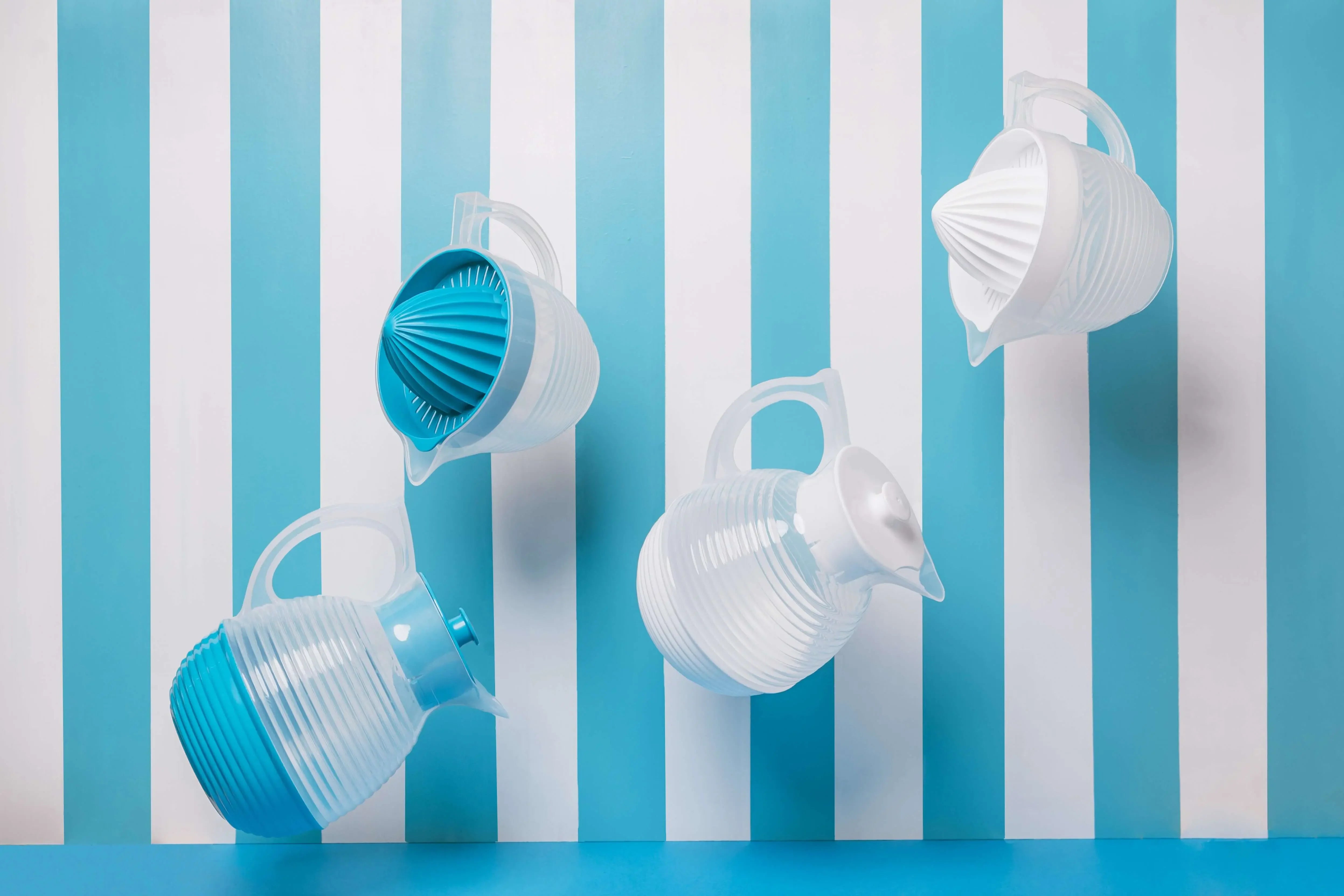 Presse-agrumes vintage en plastique bleu et blanc de fabrication française, suspendus devant un fond rayé bleu et blanc.