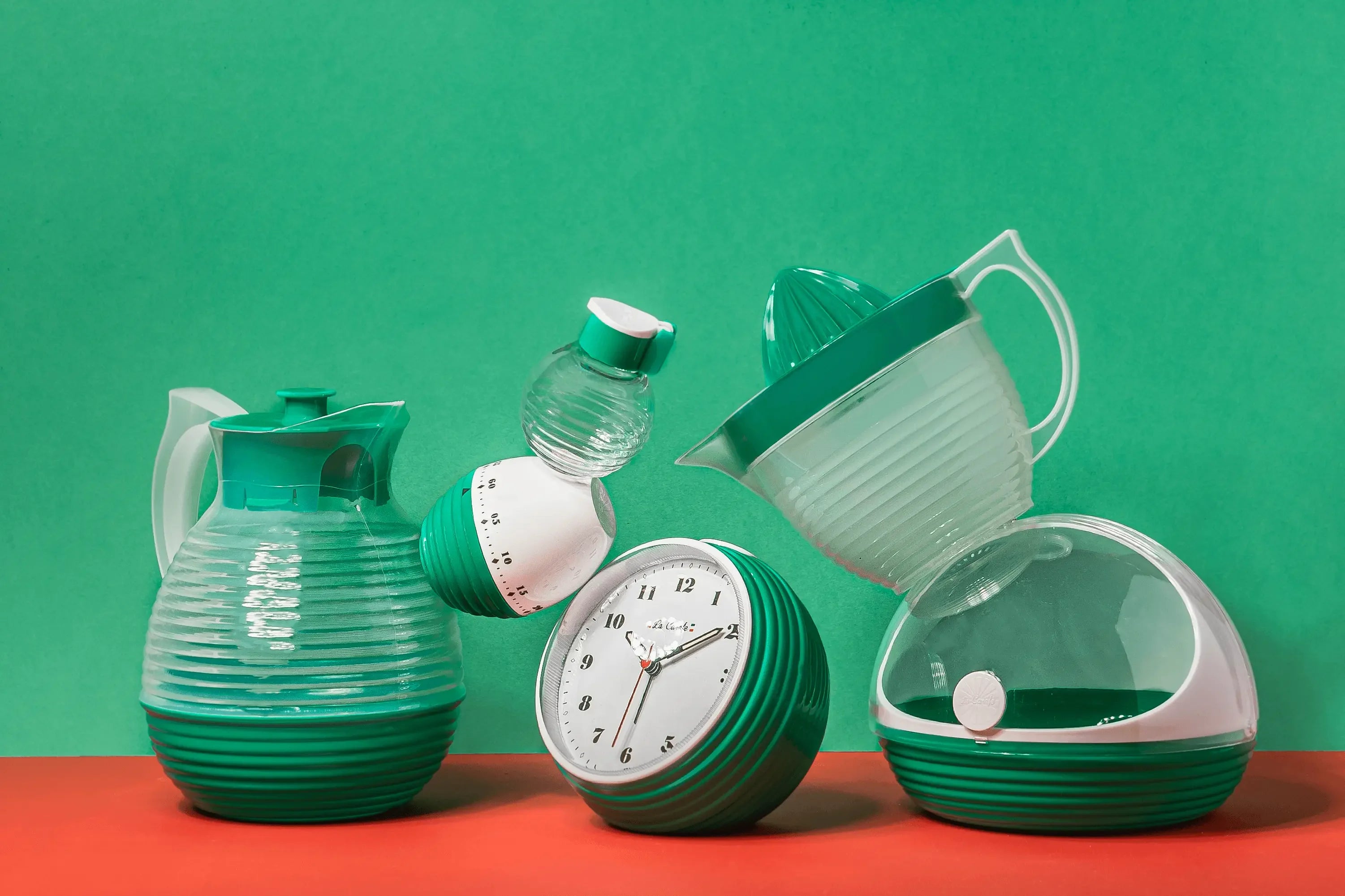 Collection rétro d'articles de cuisine verts avec carafes et accessoires vintage sur fond vert et rouge.