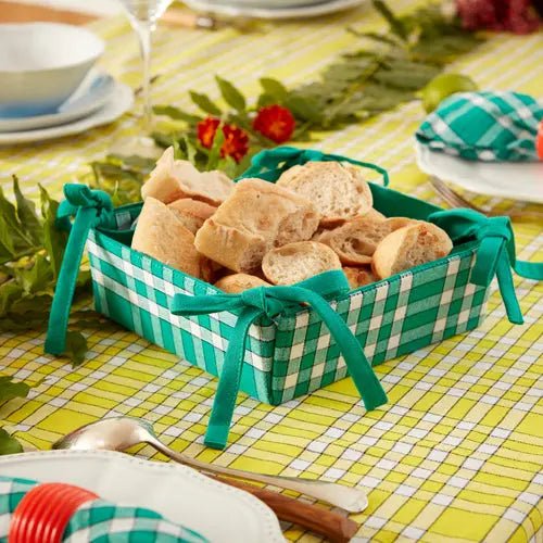 Corbeille à pain en tissu à carreaux sur une table dressée, élégante et réversible, contenant des morceaux de pain fraîchement coupés.