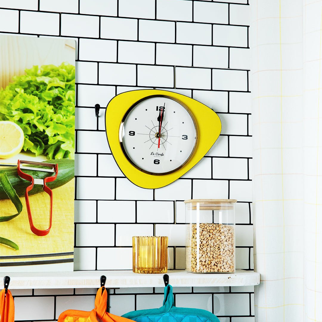 Horloge de cuisine originale jaune sur un mur en carreaux blancs, accessoire parfait pour maîtriser les temps de cuisson en cuisine.