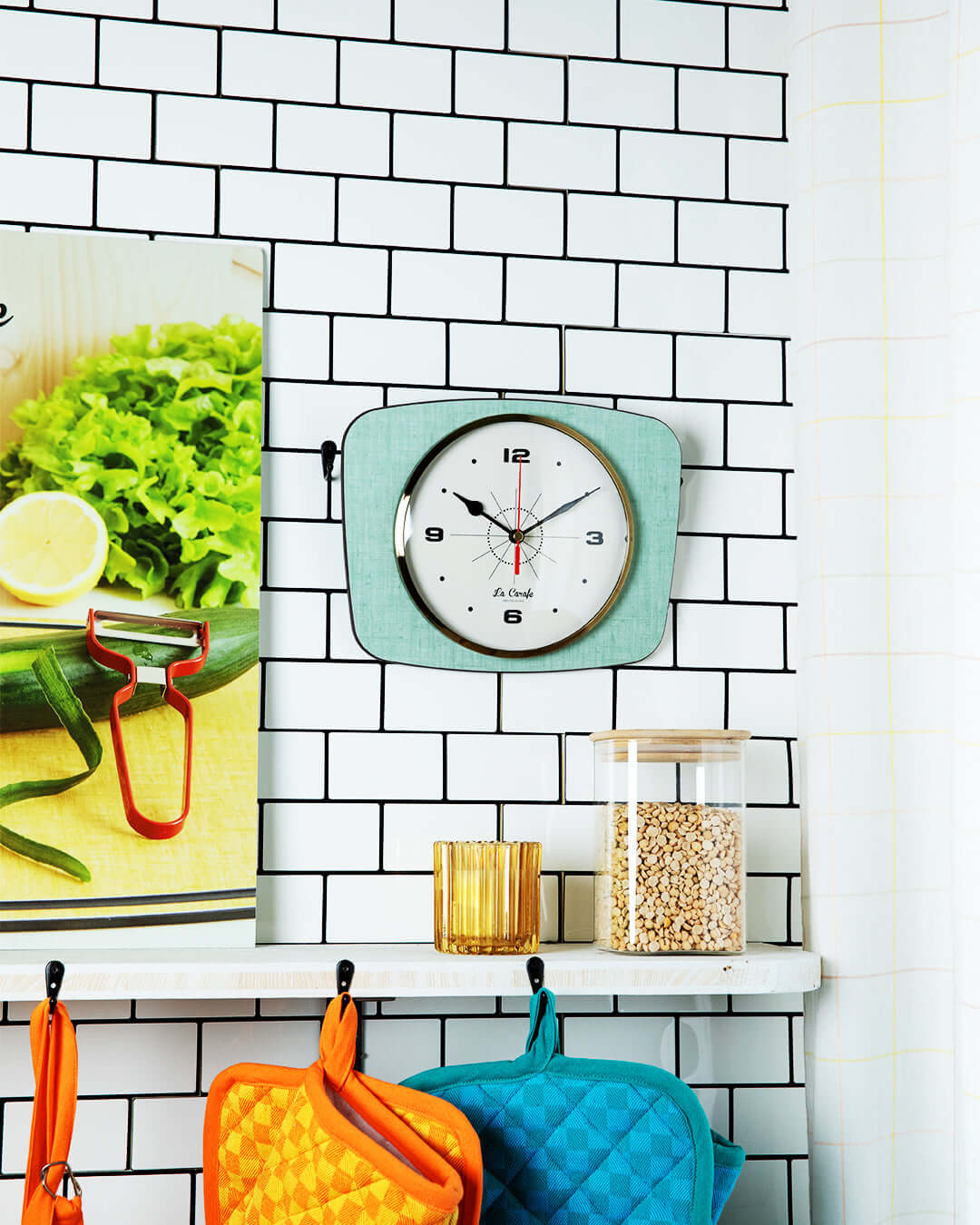 Horloge rectangulaire vintage sur un mur de cuisine avec décoration rétro et accessoires colorés.