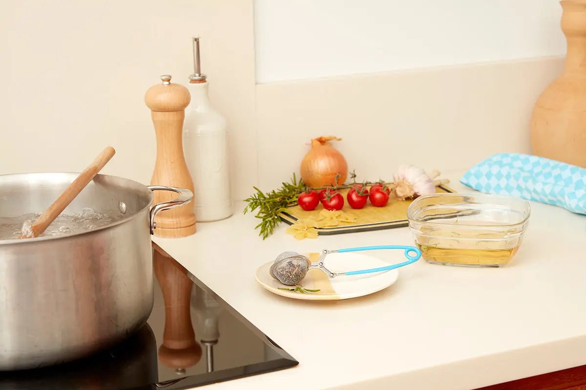 Pince à thé sur une assiette dans une cuisine moderne, près d'ingrédients frais pour infusion.