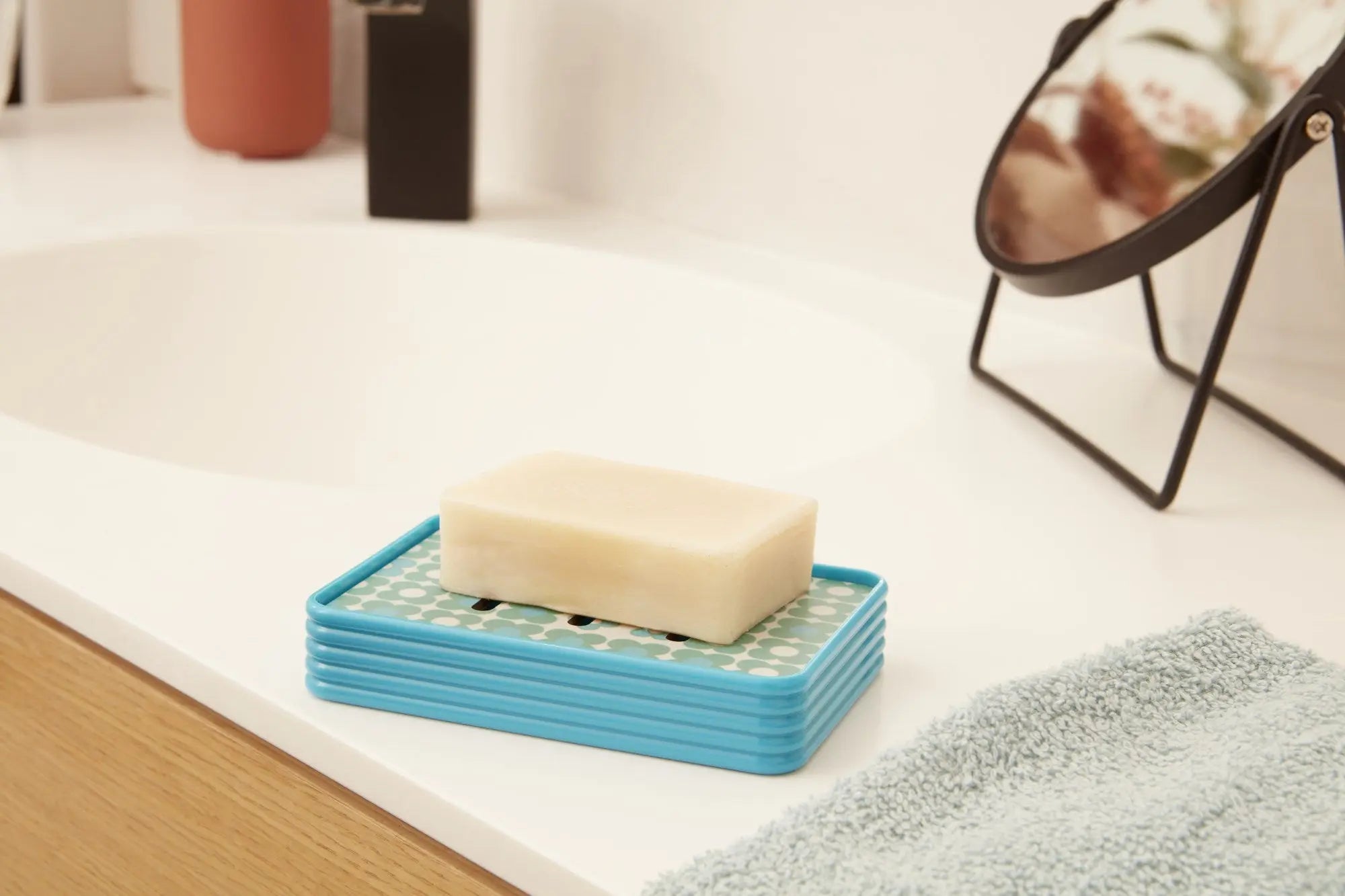 Porte-savon vintage bleu avec barre de savon sur un comptoir de salle de bain moderne, dégageant un style rétro inspiré des années 60.