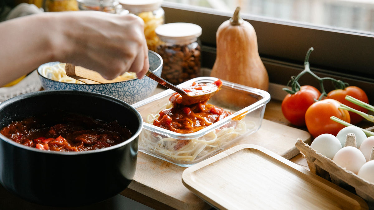 Louche versant une sauce tomate maison de la marmite vers un plat en verre, devant la fenêtre de la cuisine
