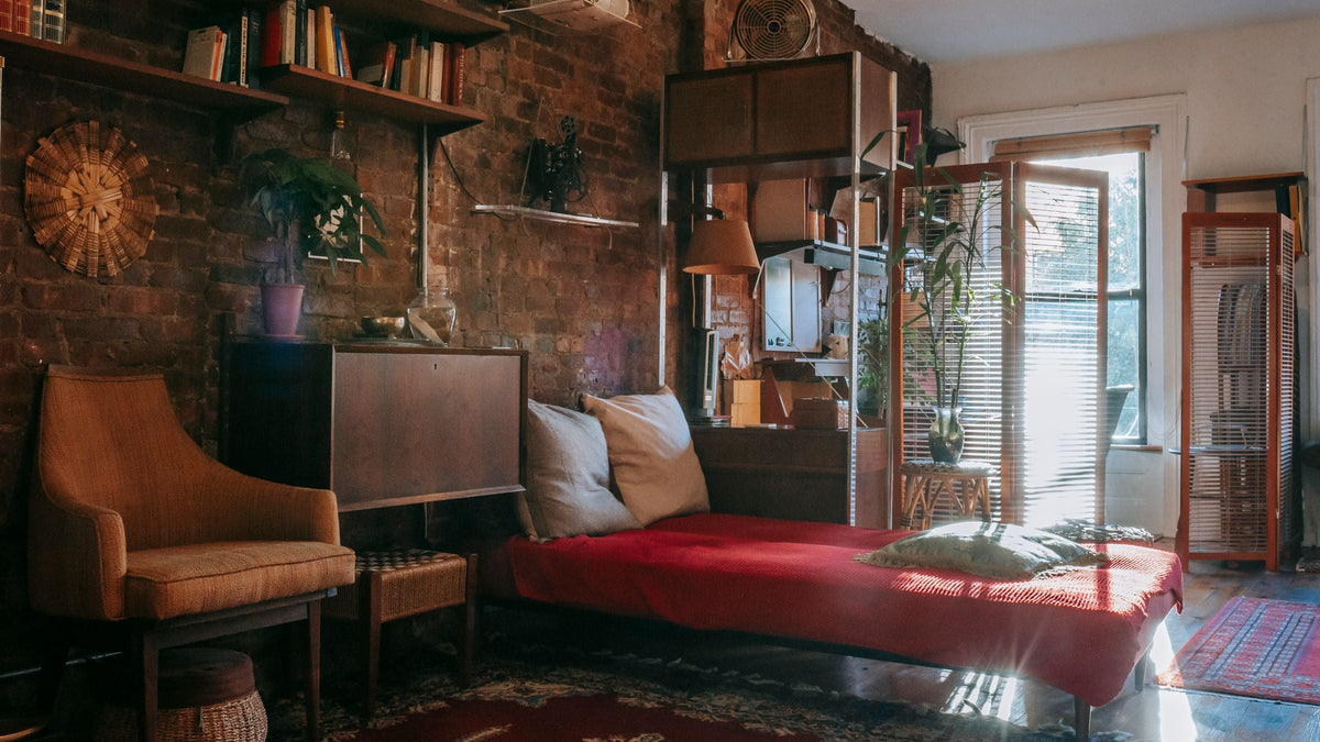 Chambre vintage baignée de lumière avec couvre-lit rouge, fauteuil rétro et meubles en bois anciens