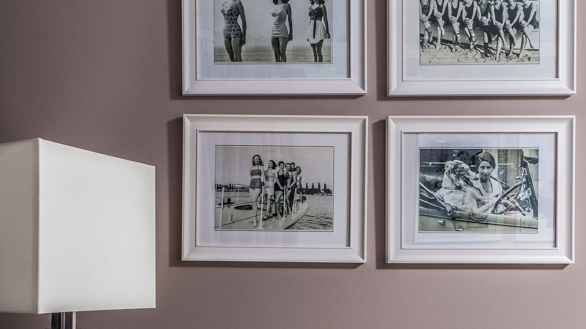 Mur de cadres vintage : quatre photographies rétro en noir et blanc encadrées de blanc sur un mur taupe
