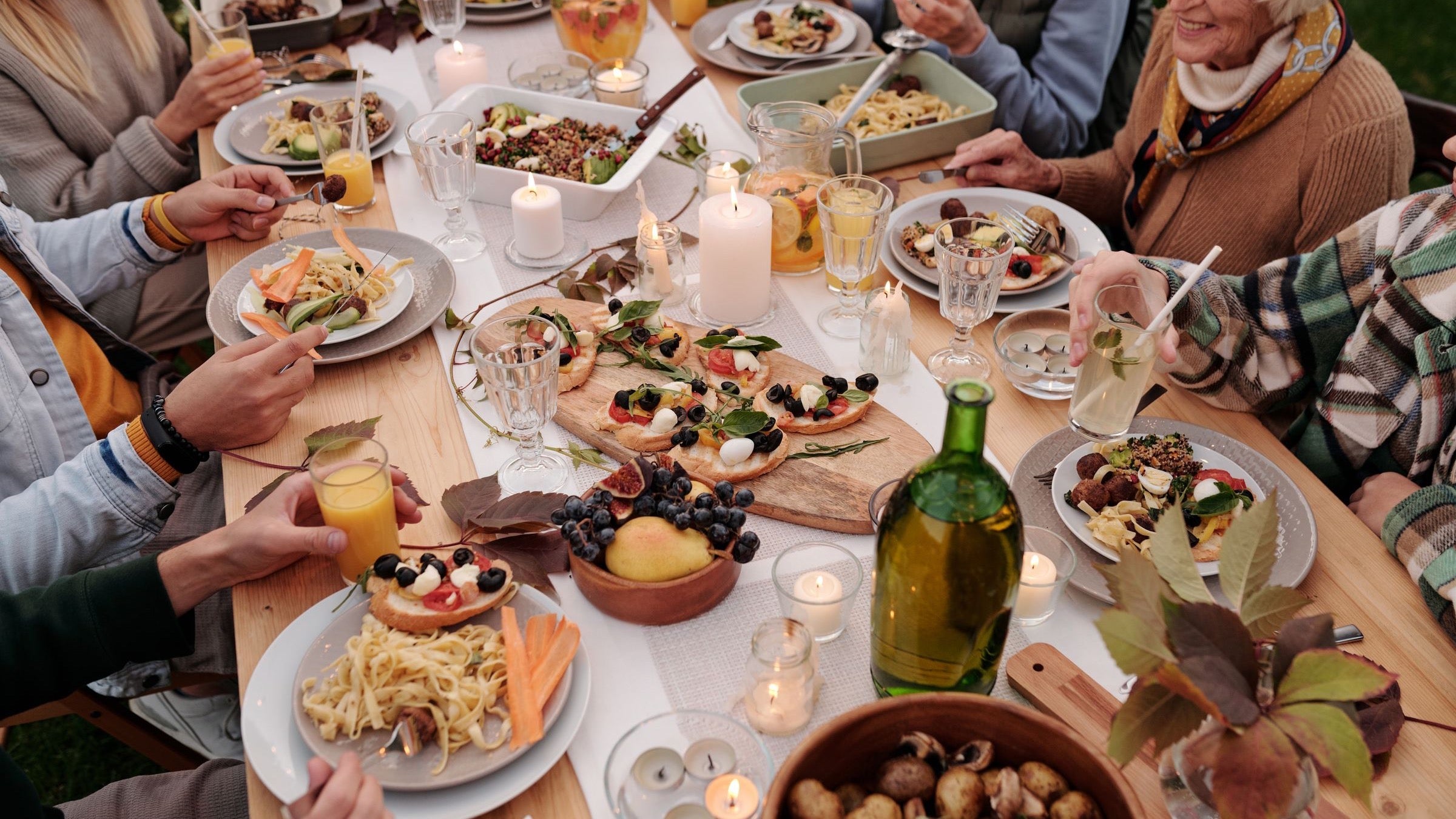 Grande tablée d'été au jardin à la tombée du soir, bougies et pichets sur la table