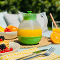 Carafe vintage en plastique vert et transparent, style années 50-70, contenant un jus orange pour décoration cuisine rétro.
